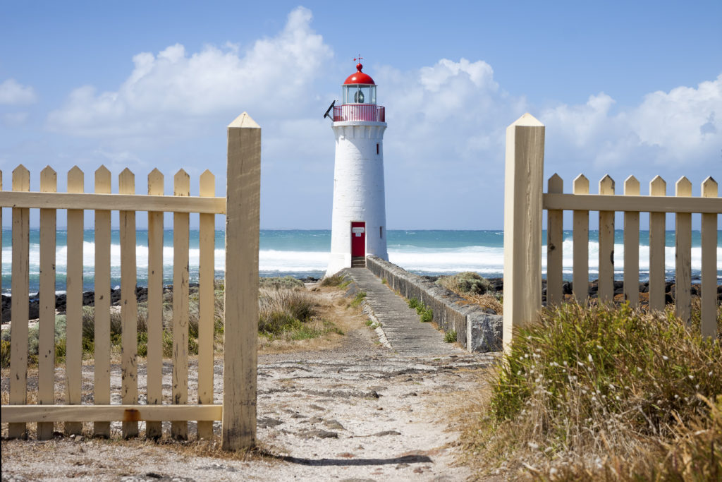 Lighthouse standing on a rocky outcrop, with a wooden fence and a path leading to it