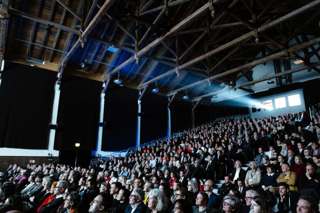 Audience watching a film in a dark cinema hall with wooden beams, during the Solothurn Film Festival.