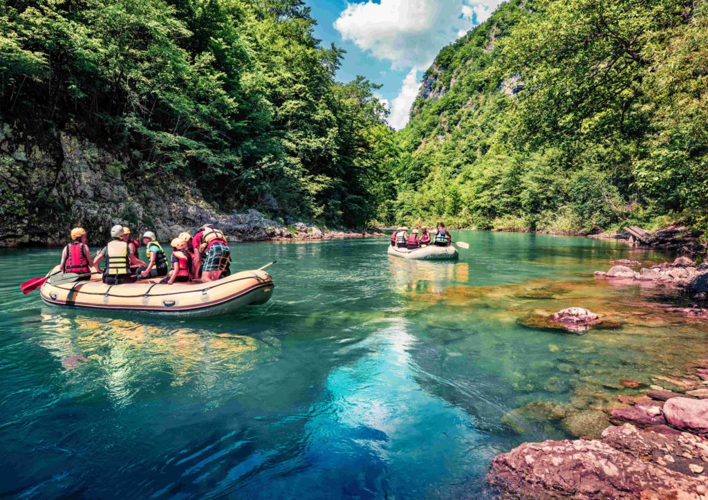 Groups rafting on a turquoise river through a lush green canyon in Montenegro.