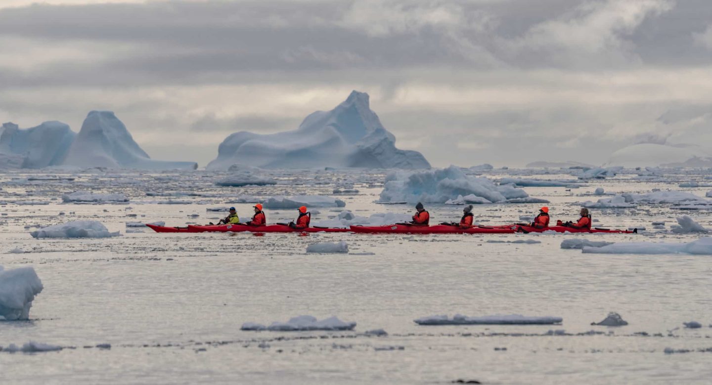 Team of adventurers in a kayak on Antarctic waters, region's unique icy environment