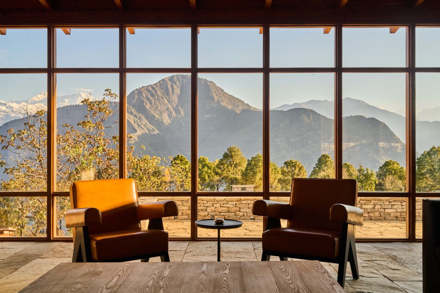 An inviting living area featuring a rustic yet modern design with a floor-to-ceiling window overlooking the Himalayas