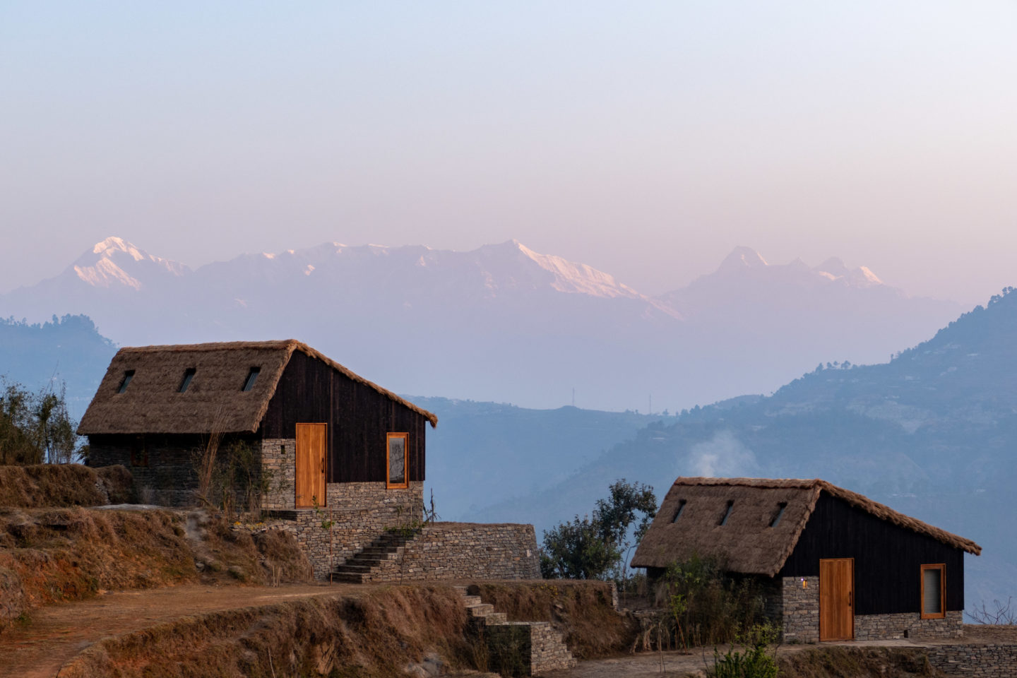 Two wooden houses perched on a hill, surrounded by mountains