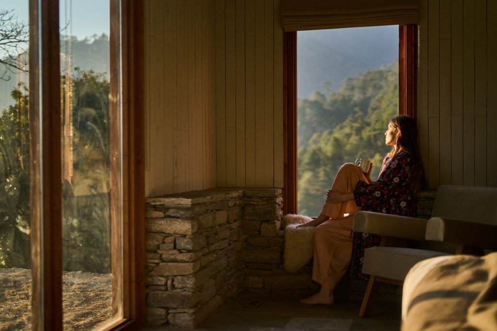 Woman relaxing indoors, bathed in warm sunlight from a window that overlooks a beautiful mountain vista