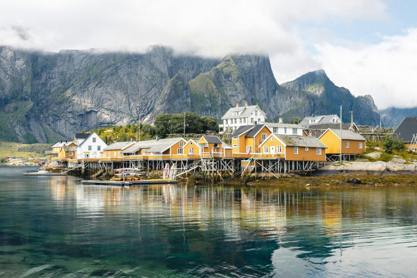 Traditional yellow and white wooden houses on stilts built over a calm fjord