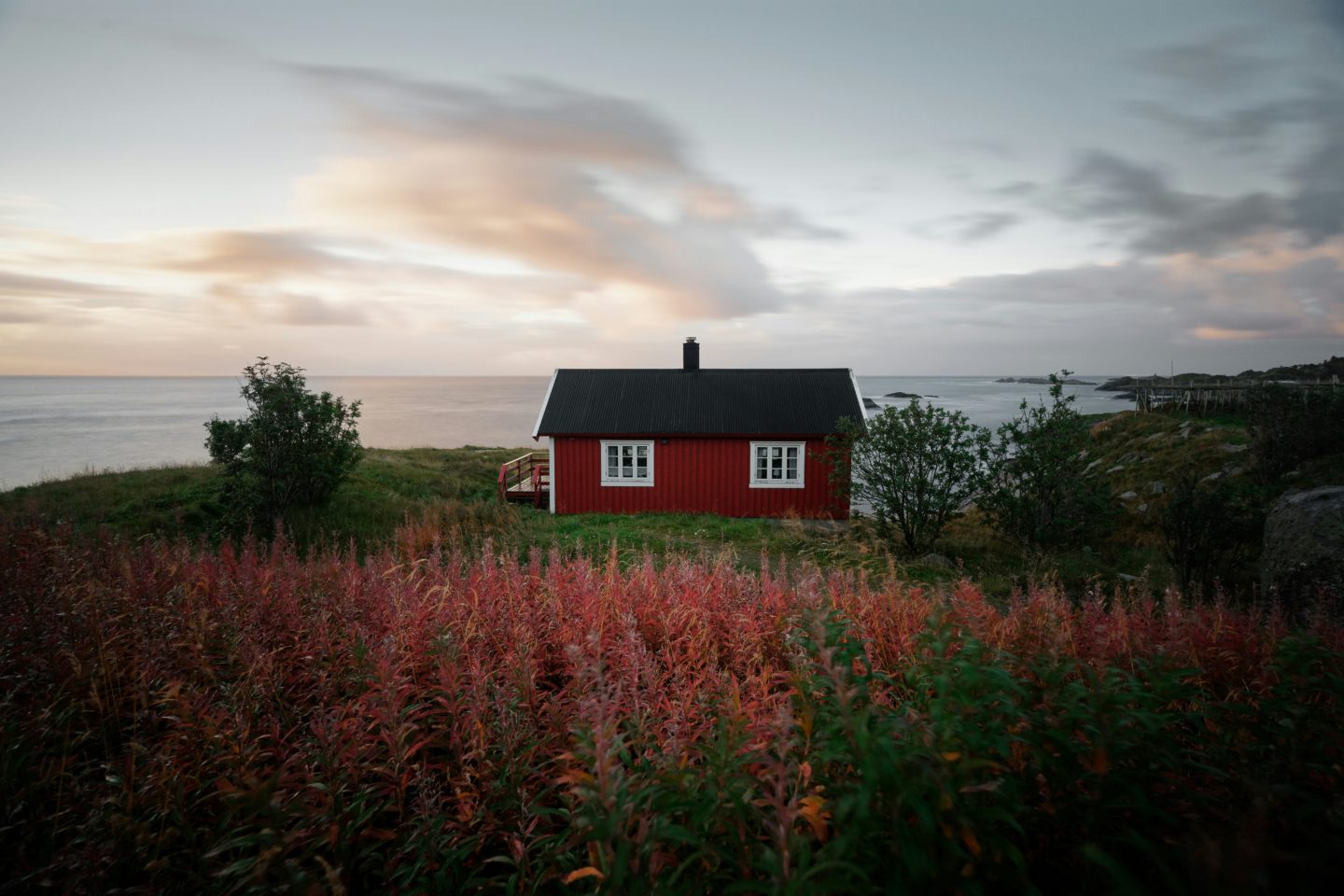 Red house with a black roof sits on a grassy hill overlooking the sea