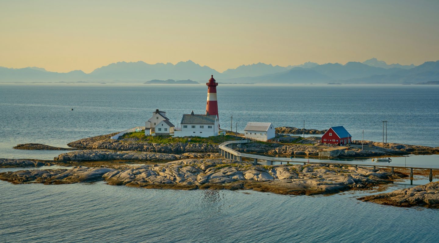 Tranøy Lighthouse stands on a rocky island in the sea, connected by a walkway to other houses