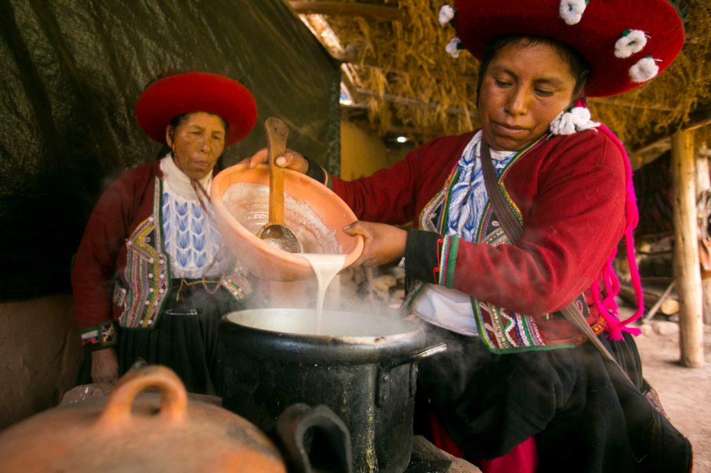 In a family kitchen, two women in traditional attire prepare causa rellena