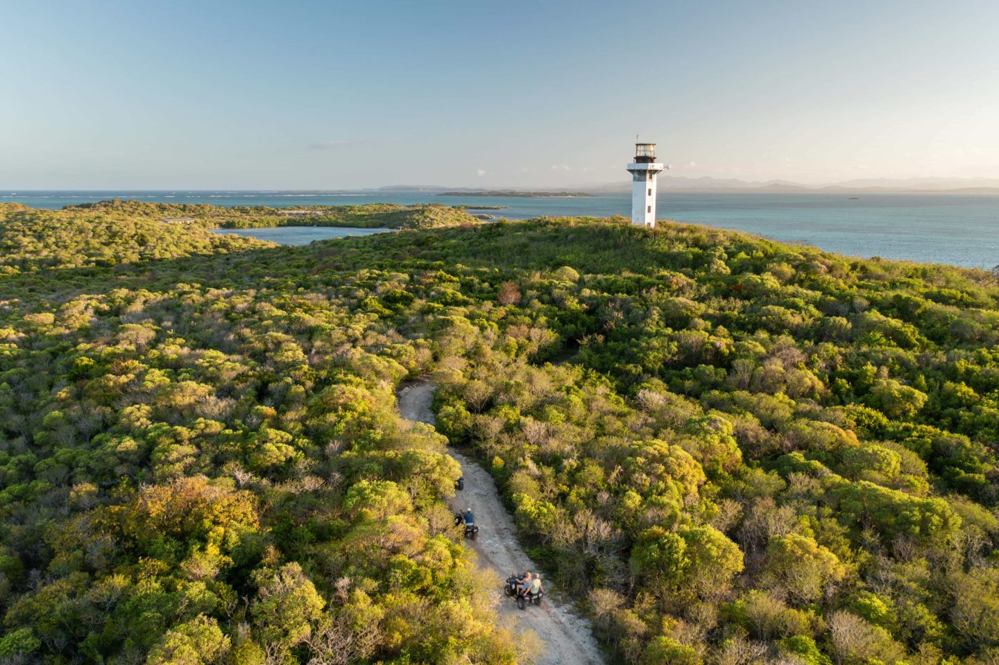 Quad biker rides towards a lighthouse on a lush green landscape in Madagascar