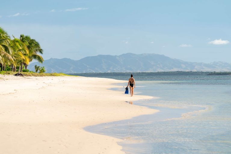 A woman walks along Miavana beach, enjoying the serene coastal scenery