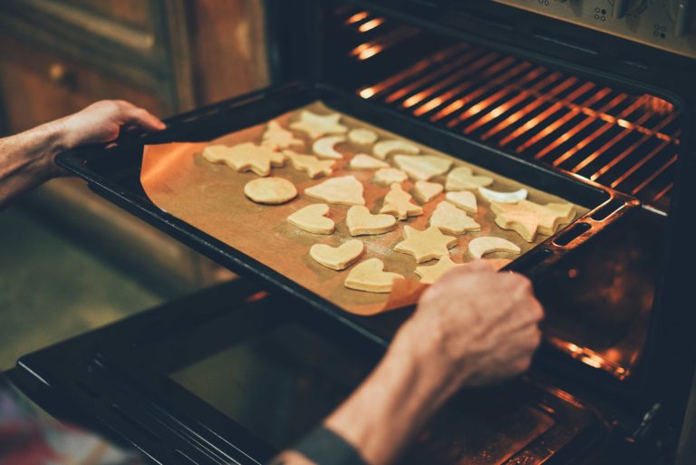 Baker placing a tray of shaped cookies in the oven
