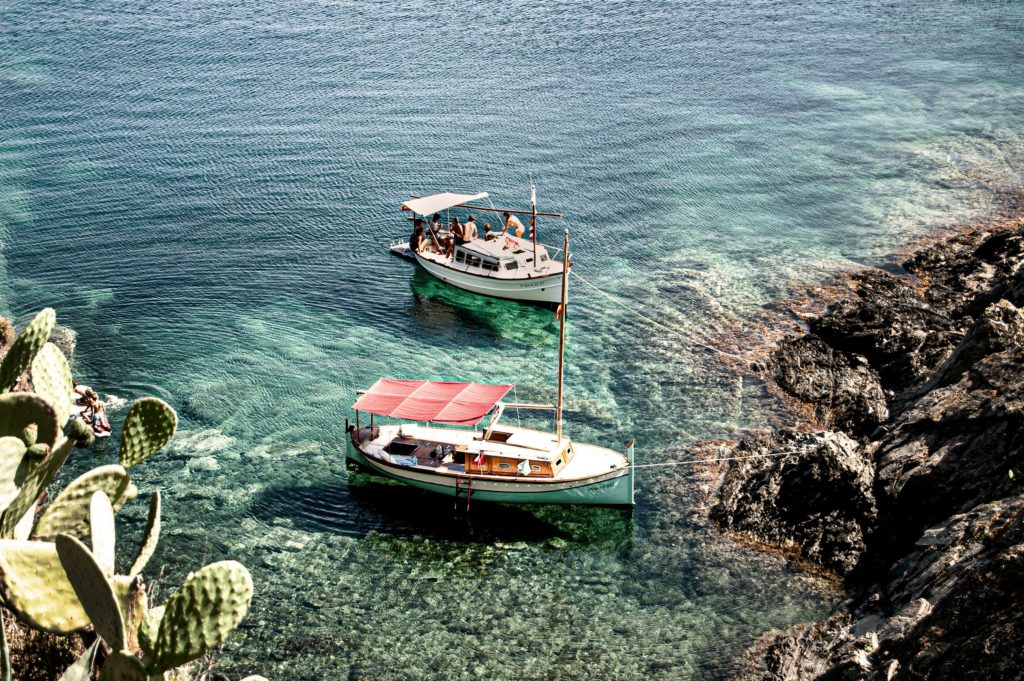 Traditional wooden boats anchored in the crystal-clear turquoise waters of a rocky Mediterranean cove.